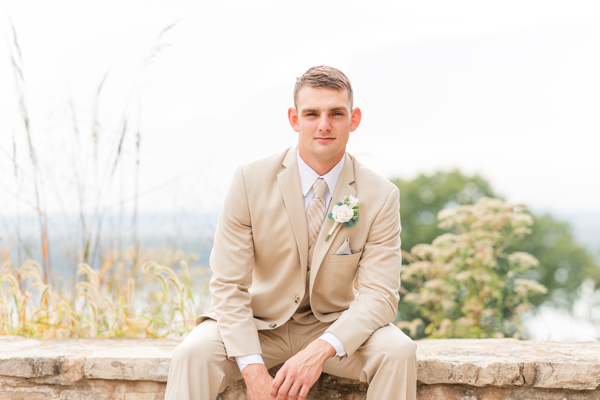 groom sits on brick wall during wedding photos