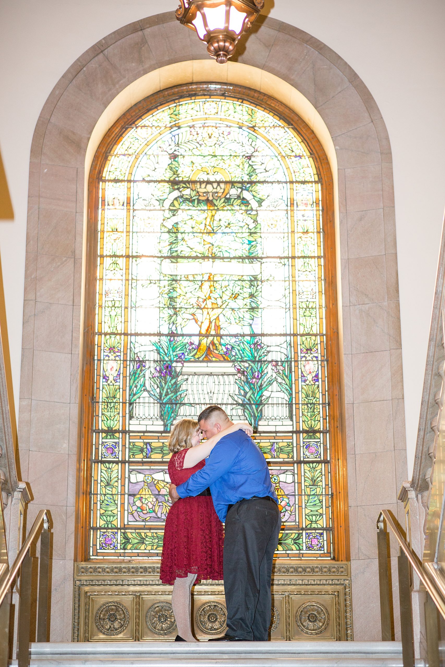 engaged couple poses b stain glass window in downtown St. Louis library at Central Library