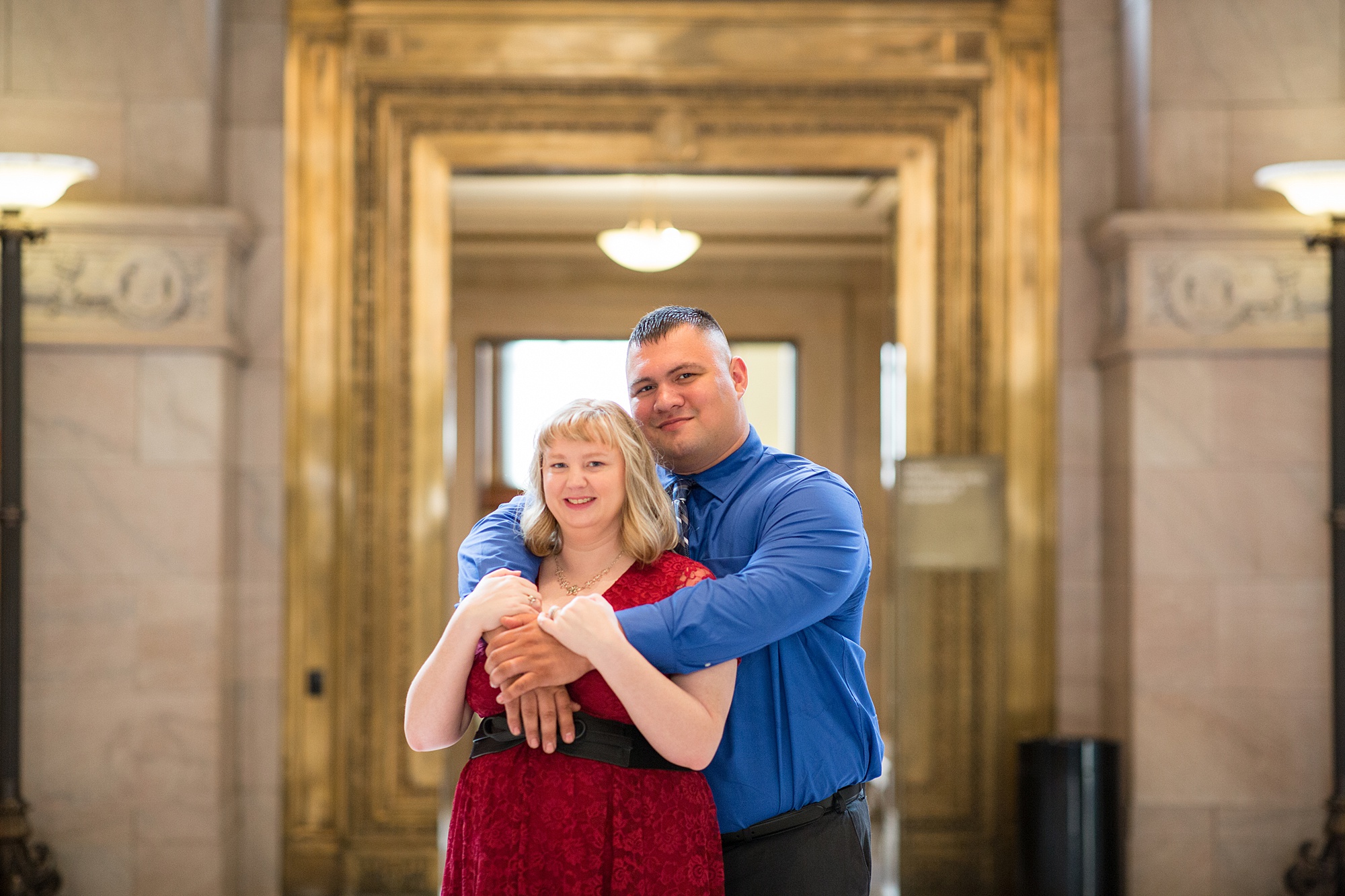 groom hugs bride from behind during engagement photos in library