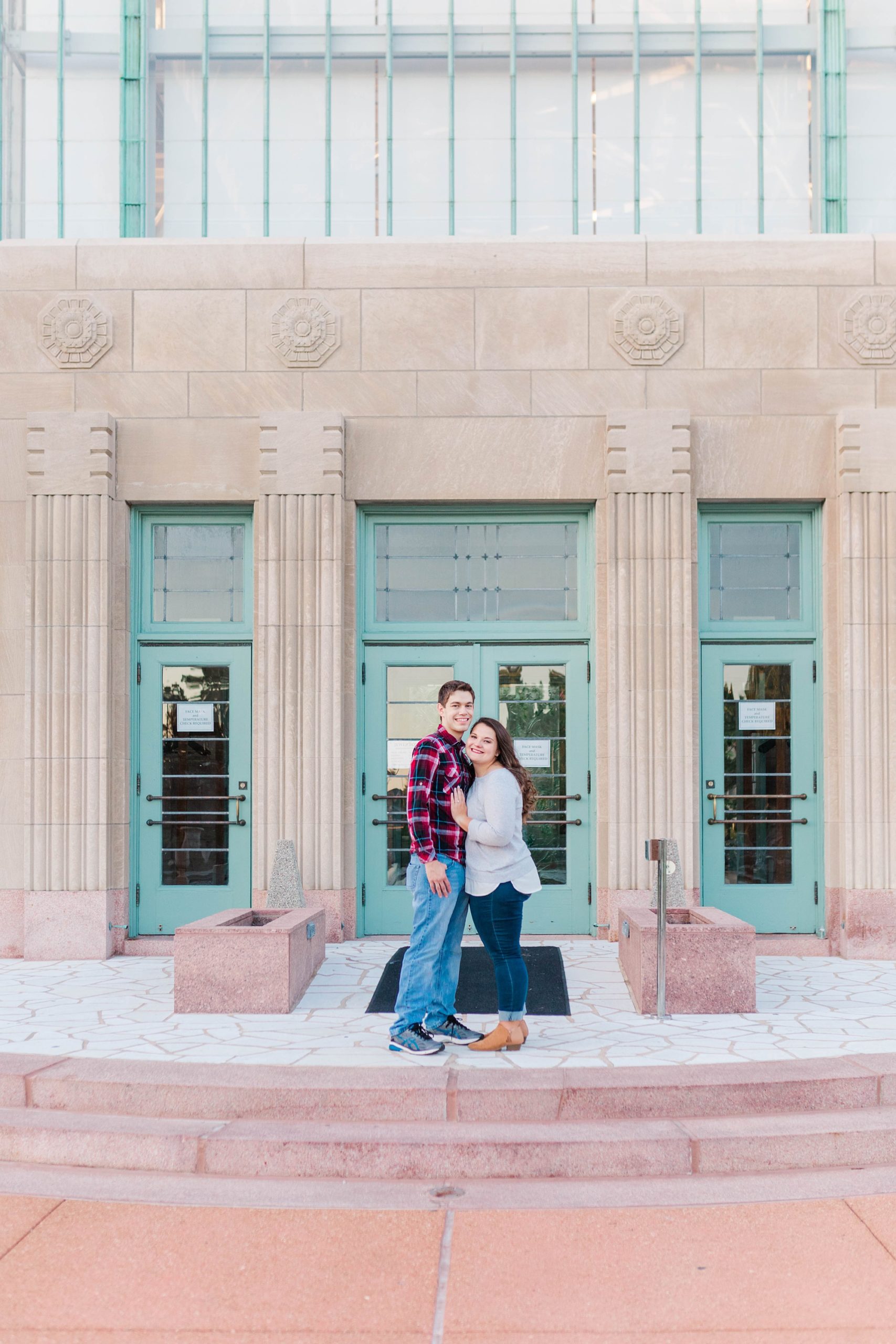 engaged couple poses by teal and concrete building