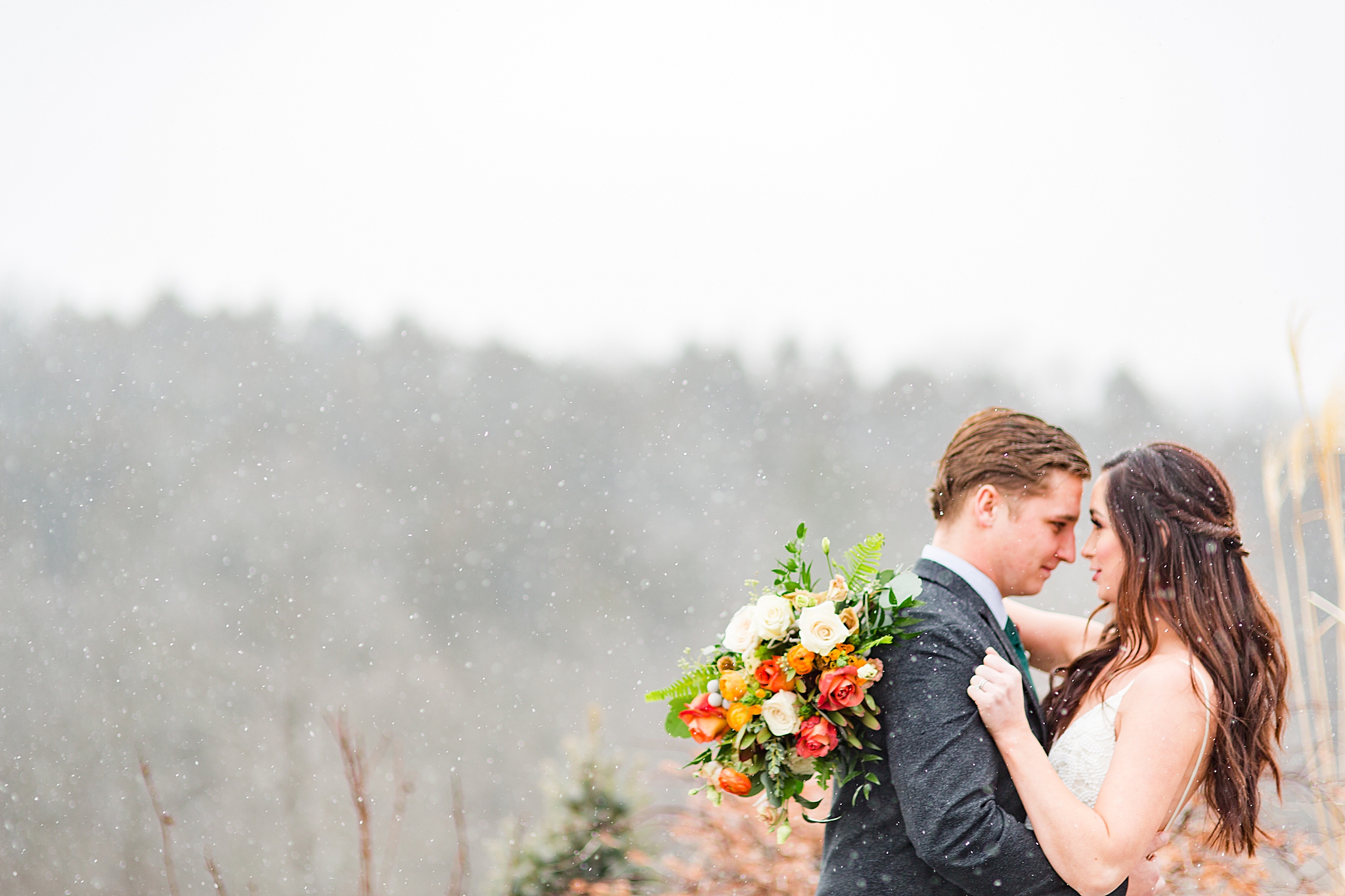 bride and groom kiss while snow falls during winter Haue Valley wedding