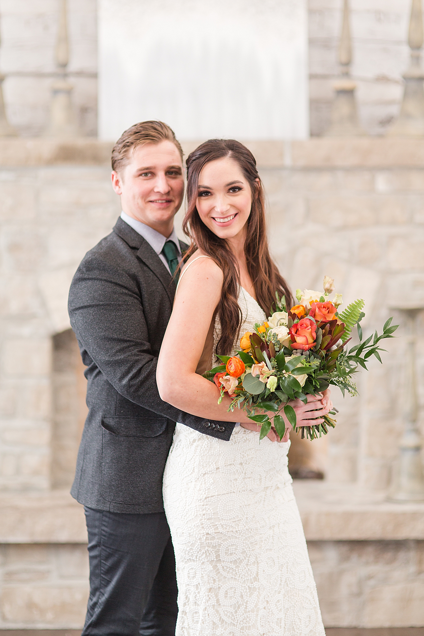 bride and groom hug standing by stone fireplace