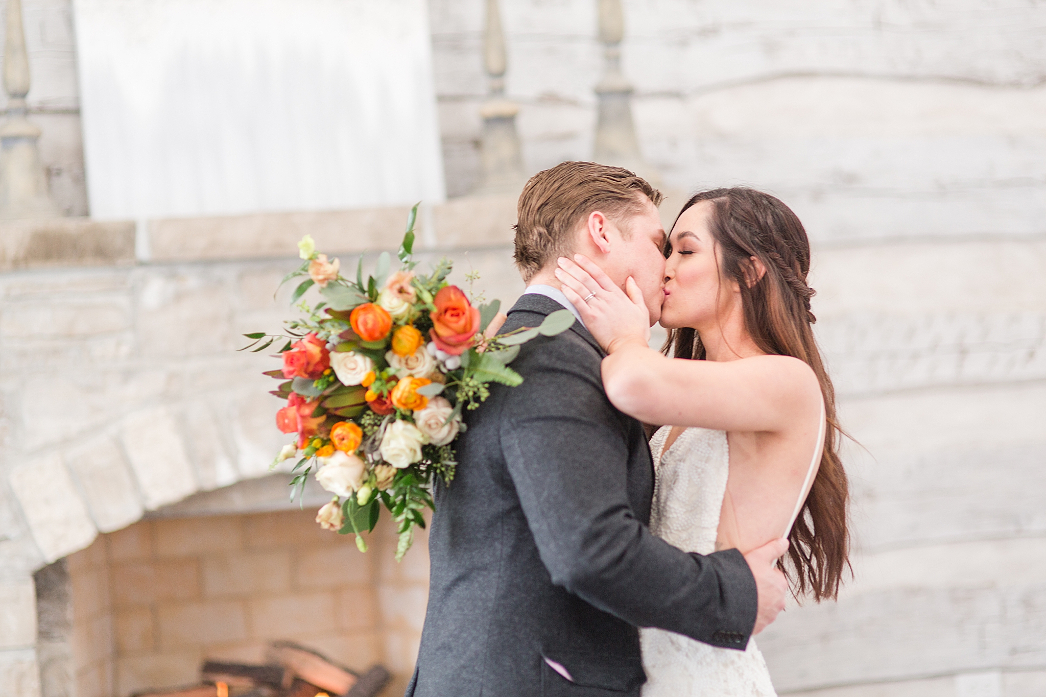 bride and groom kiss by stone fireplace