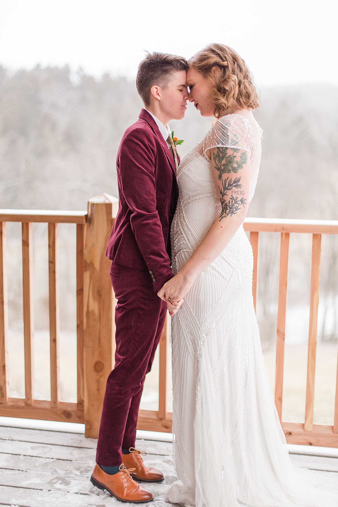 brides pose touching noses on balcony during snowy wedding portraits