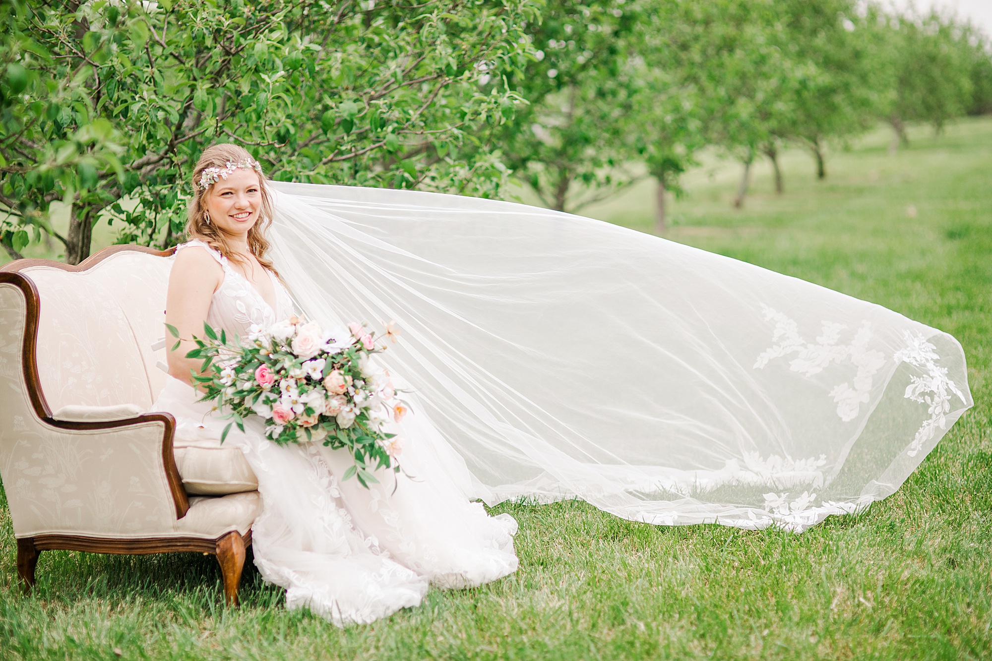 bride sits on couch with veil floating in orchard at Pierce Century Farm