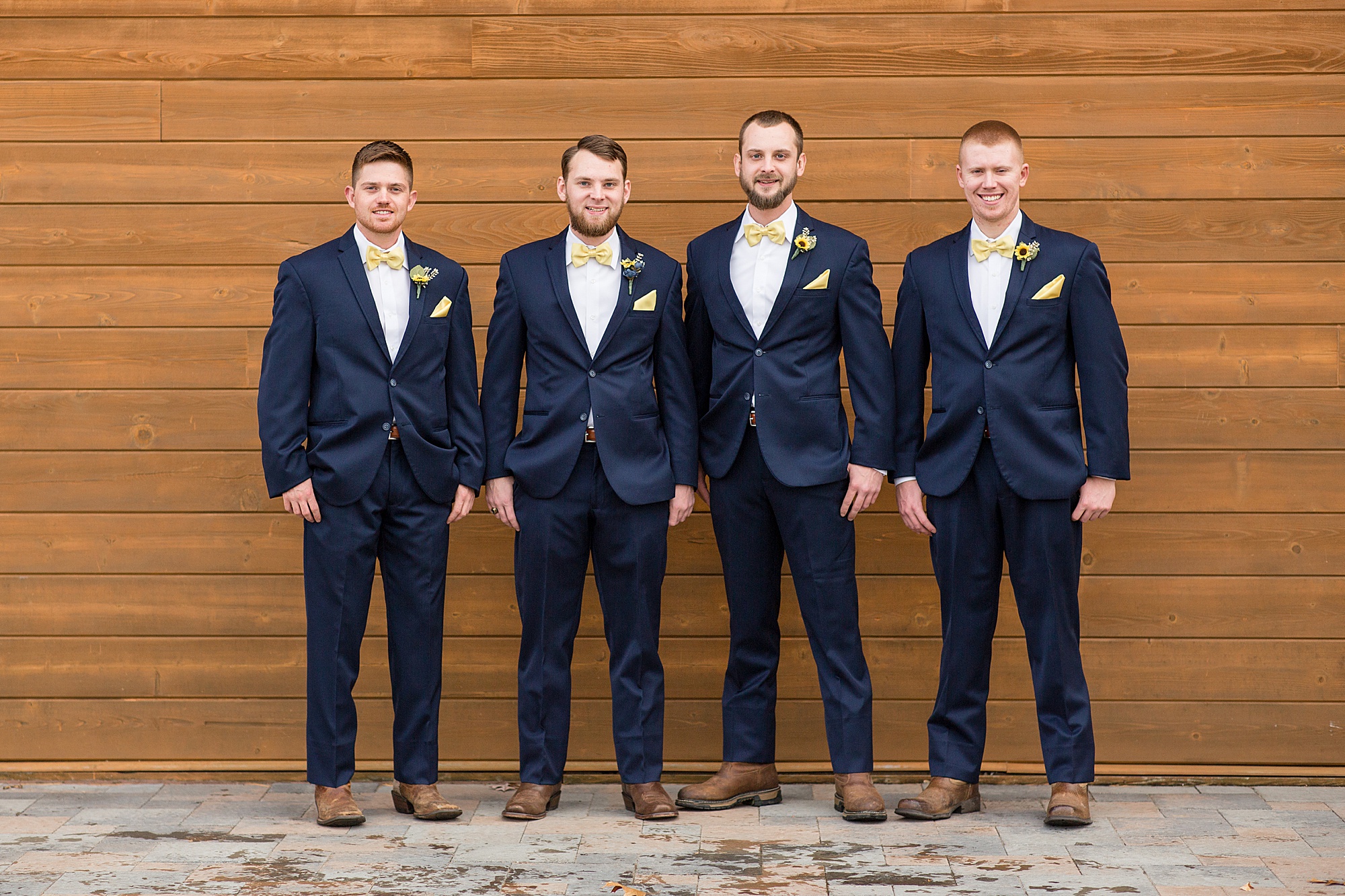 groom and groomsmen pose along wooden wall