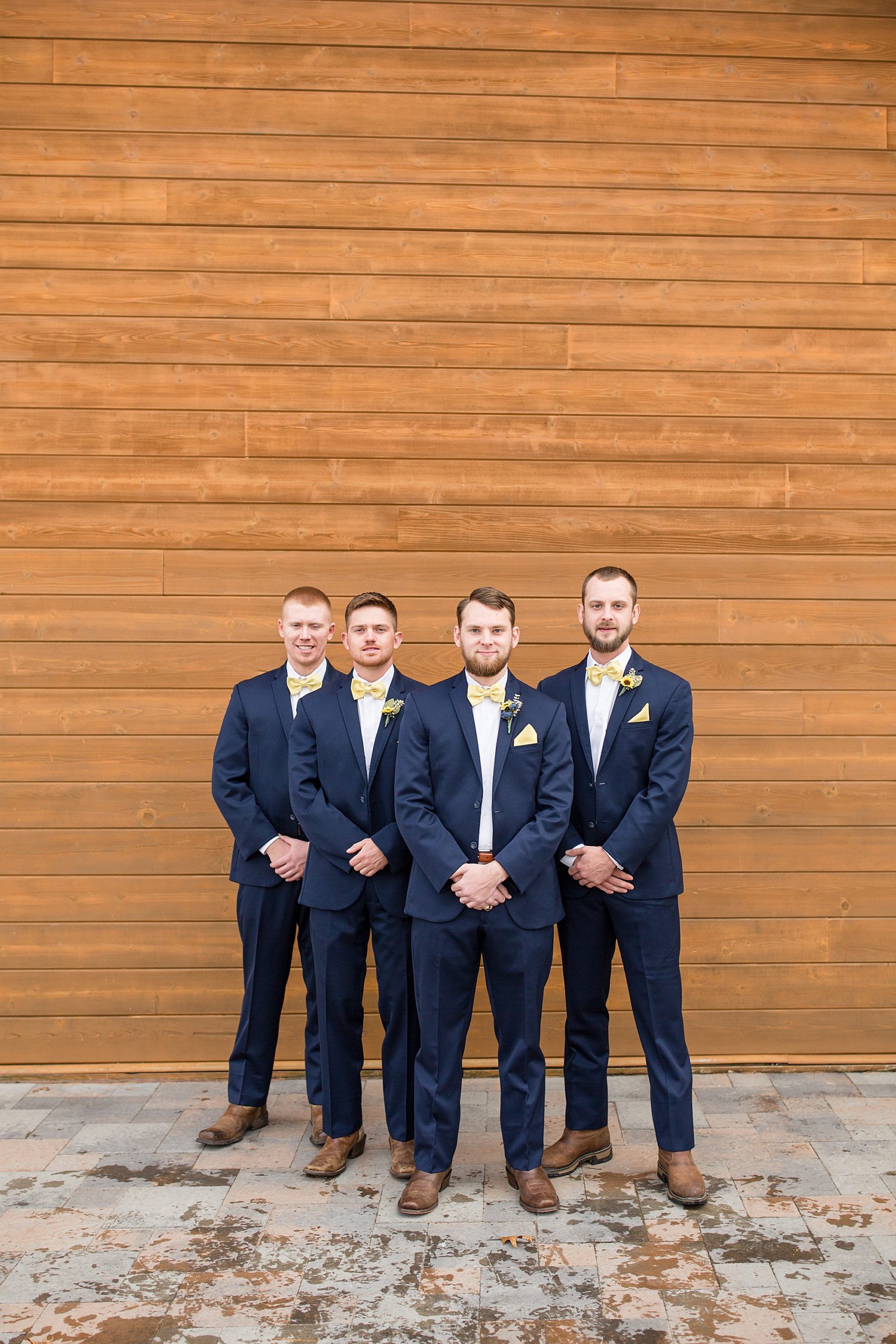 groom poses with groomsmen in navy suits outside Quail Ridge Lodge
