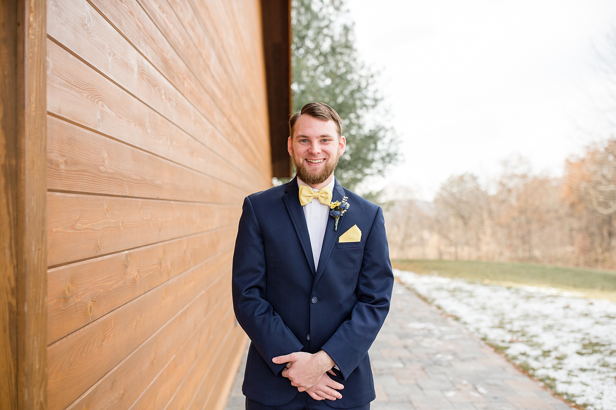 groom poses in navy suit with yellow pocket square