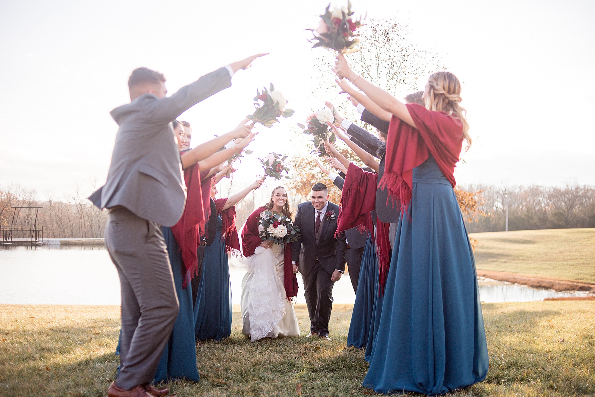 wedding party holds hands up for bride and groom to walk under