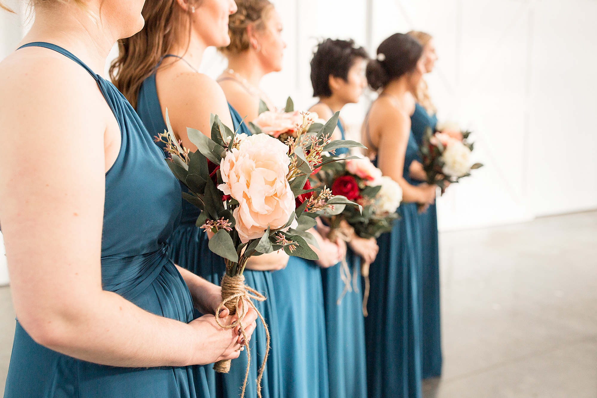 bridesmaids in teal gowns hold red and pink bouquets