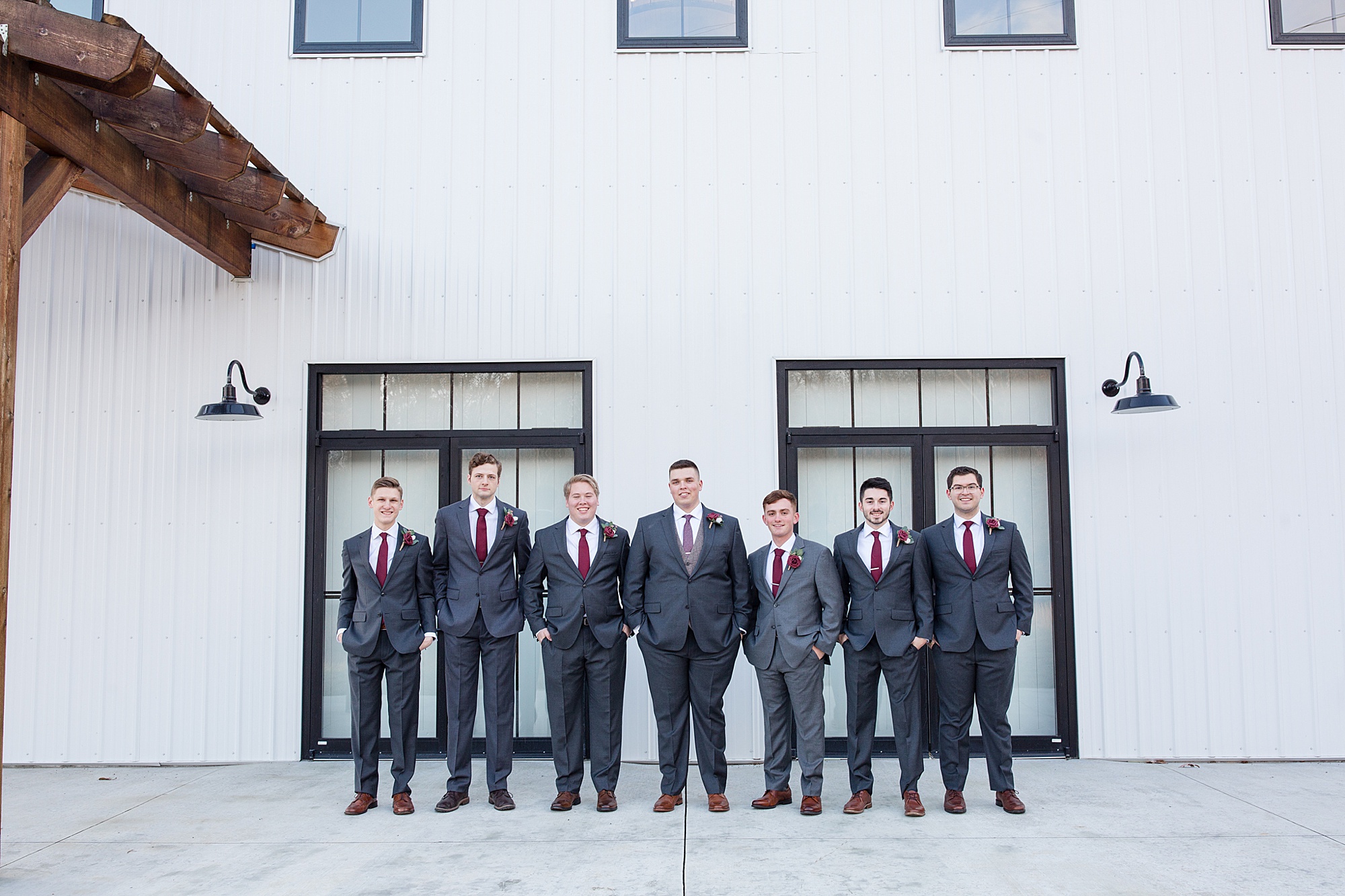 groom poses with groomsmen along white wall at Redemption Ranch