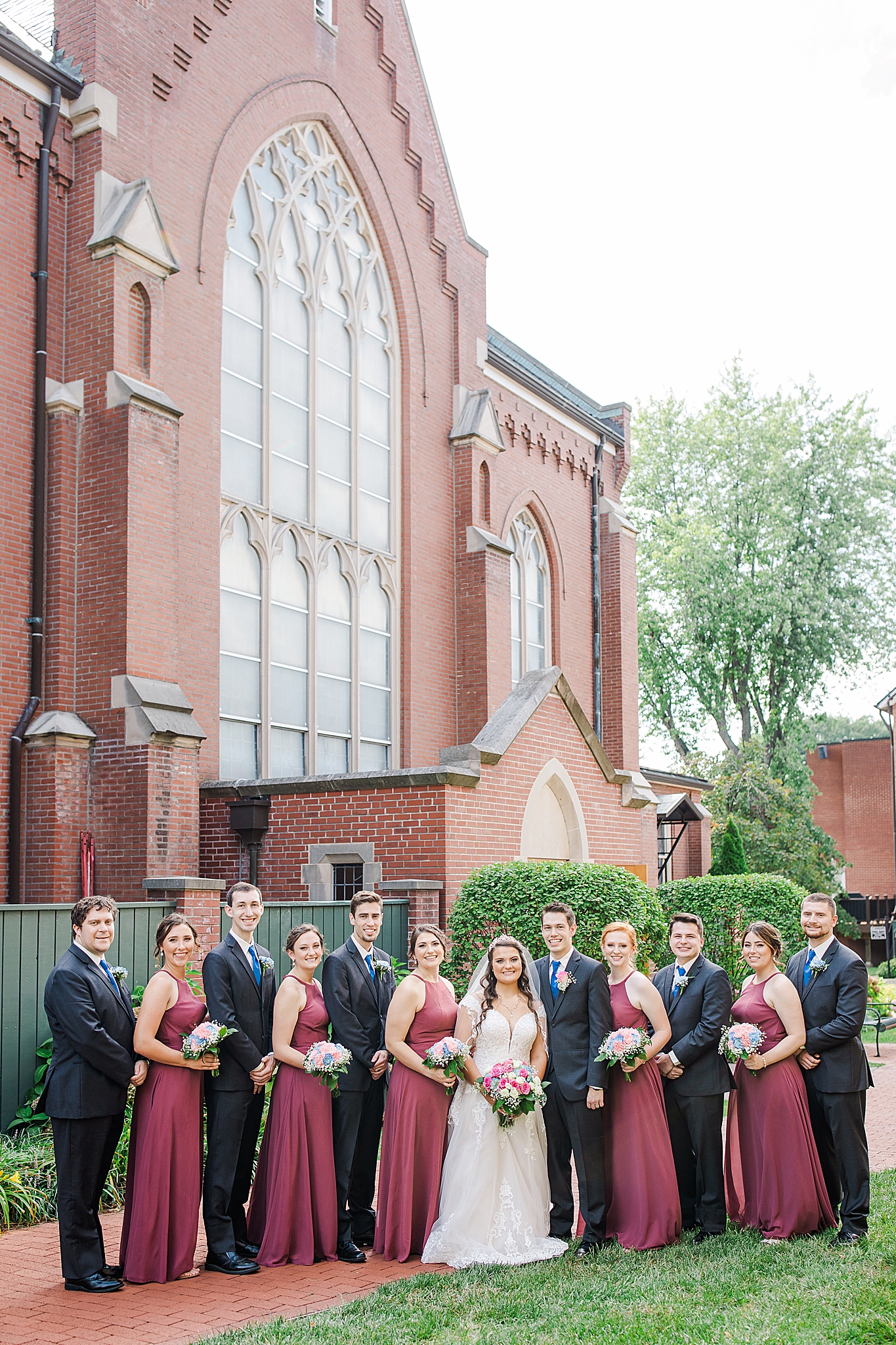 bride and groom pose with wedding party outside Sacred Heart Catholic Church of Florissant