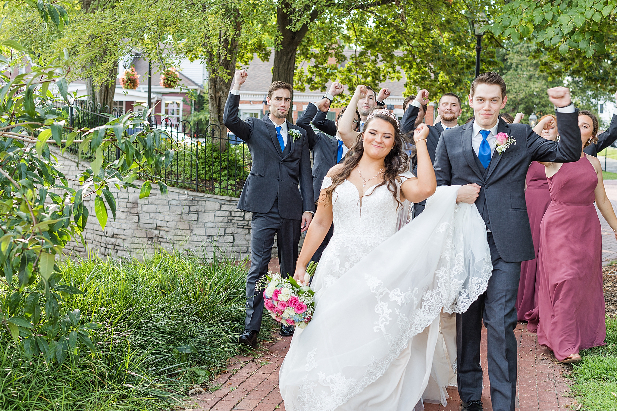 couple cheers with wedding party behind them in Missouri