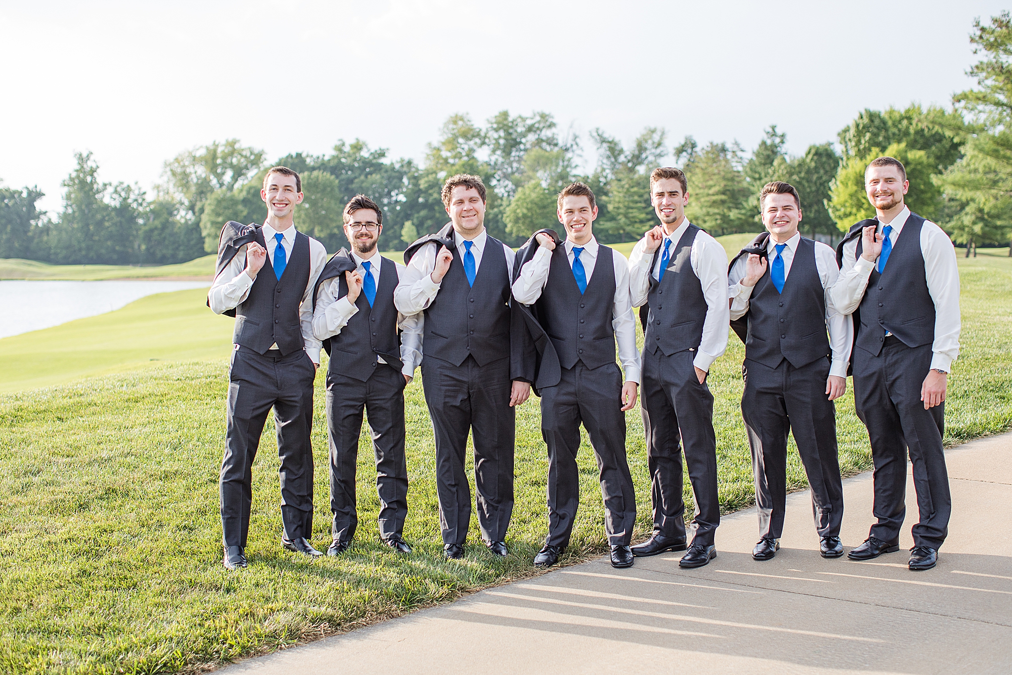 groom poses with groomsmen with jackets over shoulders