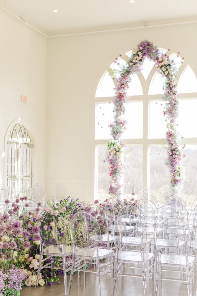 a floral arch ceremony setup including pastel purple and blush blooms inside Westwind Hills surrounded by a dramatic aisle of lush spring flowers.
