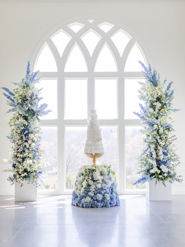 romantic wedding cake setup at Westwind Hills towering blue and purple floral cake display, and arched windows